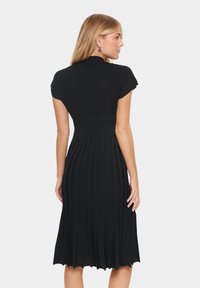 Knit black dress with short cap sleeves, fitted bodice, and pleated skirt. Features textured fabric and a knee-length hem.