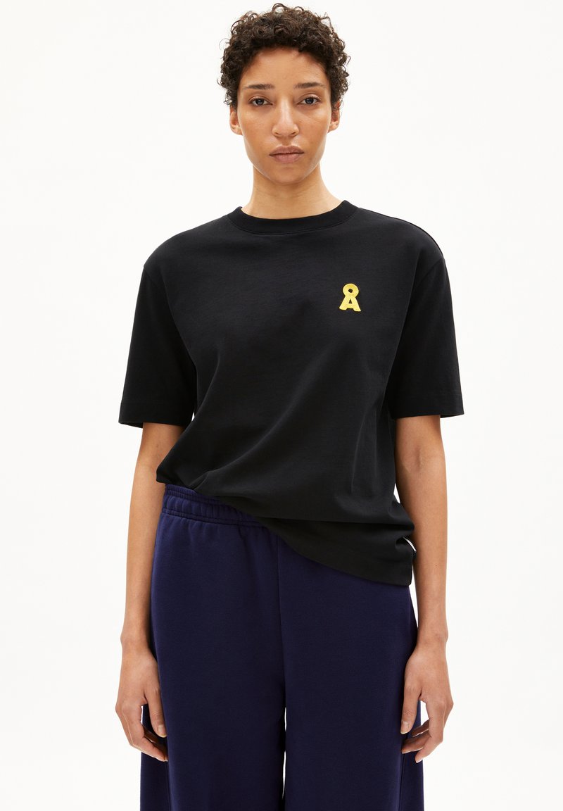 Zwart T-shirt met een gele lintontwerp op de linkerkant van de borst, gemaakt van zachte stof. Gecombineerd met loszittende marineblauwe broek.