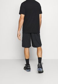 Černé sportovní tričko a černé šortky. Neformální design s volným střihem. Nosené s černými ponožkami a tmavými teniskami. Hladká textura látky.