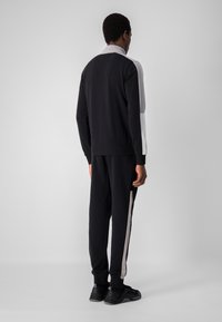 Tuta da atletica nera con design color-block con accenti grigi e bianchi. Realizzata in tessuto morbido, con polsini elasticizzati e strisce laterali.