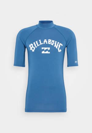 Zils īsām piedurknēm rash guard ar augstu apkakli, uz kura priekšpuses ir balta "BILLABONG" teksta un viļņa logo druka, izgatavots no elastīga auduma.