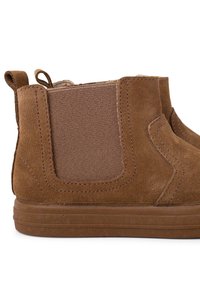 Rudos veliūro ankle batai turi elastingus šoninius panelius, lygią gumos padą ir siuvinėjimo detales; skirti lengvam avimui.