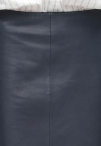 Granatowa skórzana spódnica z widocznym pionowym szwem na środku, zestawiona z białą koszulą w cienkie czarne pionowe paski.