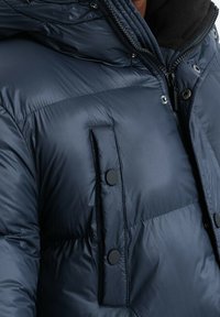 Giacca imbottita blu navy con chiusura frontale con cerniera, grandi bottoni e colletto morbido e textured. Presenta un design trapuntato per l'isolamento.