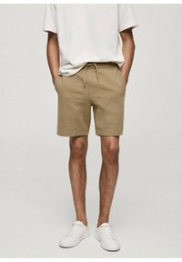 Shorts en coton beige avec une taille élastique et un cordon de serrage, dotés de deux poches latérales et d'une coupe décontractée, associés à des baskets blanches.