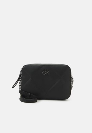 Sac bandoulière noir matelassé avec une texture lisse, des accessoires en chaîne, et un logo en relief. Il dispose d'une sangle amovible et d'une forme rectangulaire.