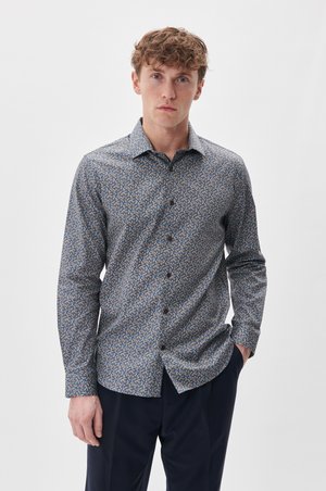 Cămașă albastră cu mâneci lungi, cu un model floral, dintr-un material moale, cu guler cu nasturi și nasturi căprui, purtată cu pantaloni negri.