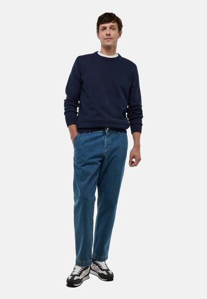 Pull en col rond navy, coupe décontractée. Jean en denim bleu clair avec une jambe droite. Baskets noir et blanc avec des détails texturés.
