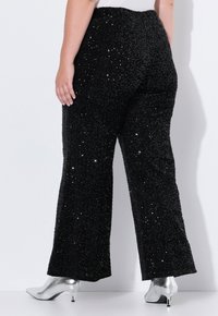 Pantaloni neri con paillettes dal superficie testurizzata, caratterizzati da un design a gamba larga e una cintura elastica, abbinati a tacchi a punta argentati.