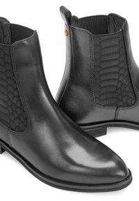Para czarnych skórzanych botków Chelsea z teksturowanymi elastycznymi panelami bocznymi i zaokrąglonymi noskami na białym tle.