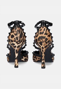 Sandalias de tacón con estampado de leopardo que presentan un upper texturizado, detalles en charol negro y un detalle de púas a lo largo del tacón y la correa del tobillo.