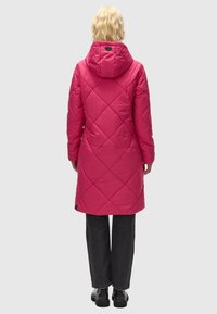 Cappotto imbottito rosa con cappuccio, motivo a losanghe, design di lunghezza media, abbinato a pantaloni scuri e stivali neri.