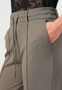 Pantalons de jogging kaki avec taille élastique, cordon de serrage ajustable, poches latérales et détails de texture subtils le long des coutures.
