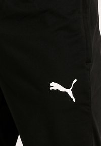Svarta träningstights med en slät yta som har en vit Puma-logotyp på vänster sida. Elastisk midja, smal passform och inga synliga fickor.