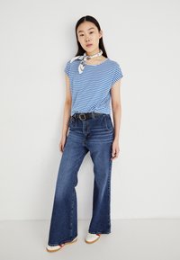 T-shirt rayé bleu et blanc avec les manches retroussées, associé à un jean en denim foncé taille haute et à jambes larges, et des chaussures blanches avec des accents rouges.