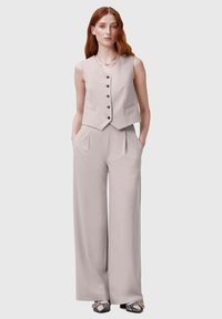 Gilet beige chiaro sartoriale con scollo a V, cinque bottoni e due tasche frontali, abbinato a pantaloni a gamba larga realizzati nello stesso materiale e colore.