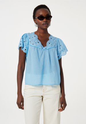 Helle blaue Bluse mit kurzen, gepufften Ärmeln und gewellter Piquée-Stickerei am Ausschnitt. Kombiniert mit hellen Hosen.