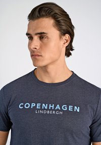 Mörkgrå bomullströja med korta ärmar som har "COPENHAGEN LINDBERGH" tryckt i ljusblå bokstäver över bröstet.