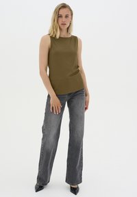 Top senza maniche verde oliva con una texture a coste, abbinato a jeans grigi a vita alta con gamba svasata e tacchi neri a punta.