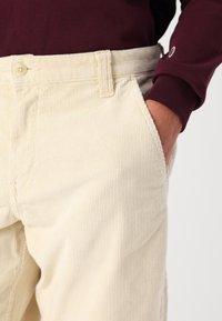 Pantaloni in corda beige con superficie tessurizzata, caratterizzati da un design a taglio dritto, tasche laterali e chiusura con bottone in vita.