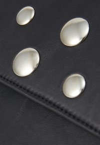Gros plan sur une surface noire texturée avec quatre boutons métalliques ronds et brillants, rehaussant un accessoire élégant.