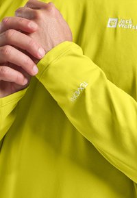 Limoengroene langemouwshirt met gestructureerde stof. Beschikt over een logo op de borst en "TEXAPAT" geborduurd op de manchette van de mouw.
