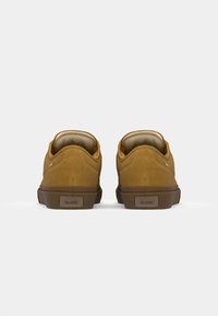Brown suede shoes with a low profile, rounded shape, and a textured rubber sole. Features a logo on the heel and a padded collar.
