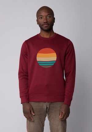 Bordeaux hoodie met een ronde grafische print met oranje, gele en teal horizontale strepen. Zachte textuur en ronde halslijn.