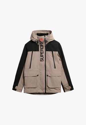 Lichtgewicht gewatteerd jack in beige en zwart, met ritszakken, een opvallend logo op de borst en verstelbare trekkoorden aan de kap.