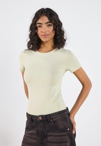 Camiseta de manga corta ajustada verde claro, hecha de tela suave, con un escote redondo y combinada con unos pantalones vaqueros oscuros de tiro alto.