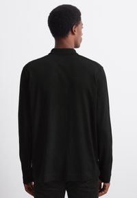 Black long-sleeve polo shirt made of soft fabric with a relaxed fit, featuring a collar and stitched hem, viewed from the back.