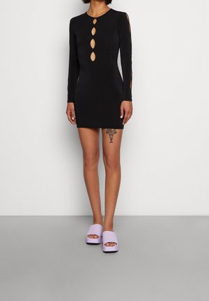 Czarna sukienka z długim rękawem z wycięciami w kształcie owalów z przodu i po bokach; dopasowany krój. W połączeniu z lawendowymi klapkami na płaskiej podeszwie. Gładka tekstura materiału.