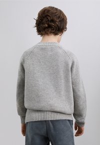 Suéter gris de punto con cuello redondo y dobladillo acanalado; cuenta con mangas ranglán y una textura suave; combinado con pantalones de pana azul.