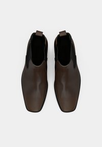 Καφέ δερμάτινα slip-on παπούτσια με λείο φινίρισμα, στρογγυλή μύτη, αντίθετες ελαστικές πλευρές και ταβερνόχέρι πίσω για εύκολη χρήση.