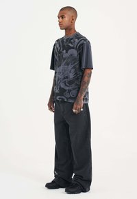 Short-sleeve, black graphic t-shirt with a detailed dark design, paired with loose-fitting black jeans and black sneakers.