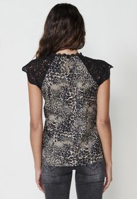Maniche a cappuccio in pizzo nero con un corpo a stampa leopardata in beige e nero. Il retro presenta un'apertura a chiave con chiusura a bottone.