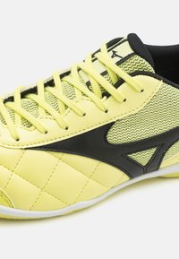 Zapatilla deportiva amarilla con parte superior sintética texturizada, paneles de malla, acentos negros y un diseño acolchado en la zona de los dedos.