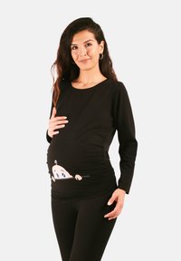 Schwarzes langärmliges Stilloberteil mit einem Cartoon-Babymotiv am Bauch und Raffung für einen figurbetonten Look. Kombiniert mit schwarzen Leggings.