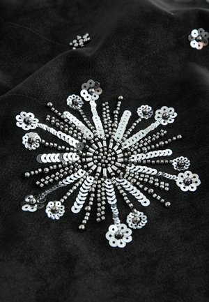 Black fabric featuring intricate silver sequins arranged in a sunburst pattern, with varying sizes of beads and flower-like designs embedded.