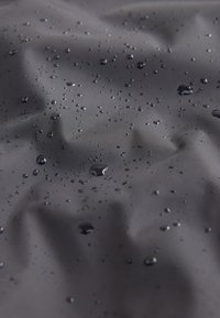 Des gouttes d'eau perlent sur un tissu imperméable gris foncé avec une texture visible et de légères rides.