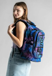 Zaino colorato con un motivo a foglia tropicale in tonalità di blu e viola. Presenta accessori neri e spallacci regolabili per il massimo comfort.