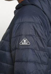Navy puffer jacket featuring a quilted design, soft texture, and a triangular logo patch on the left shoulder.