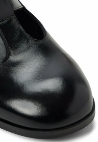 Černá kožená bota s hladkým, lesklým povrchem, se zářezy na bocích a zaoblenou špičkou. Minimalistický design bez akcentů.