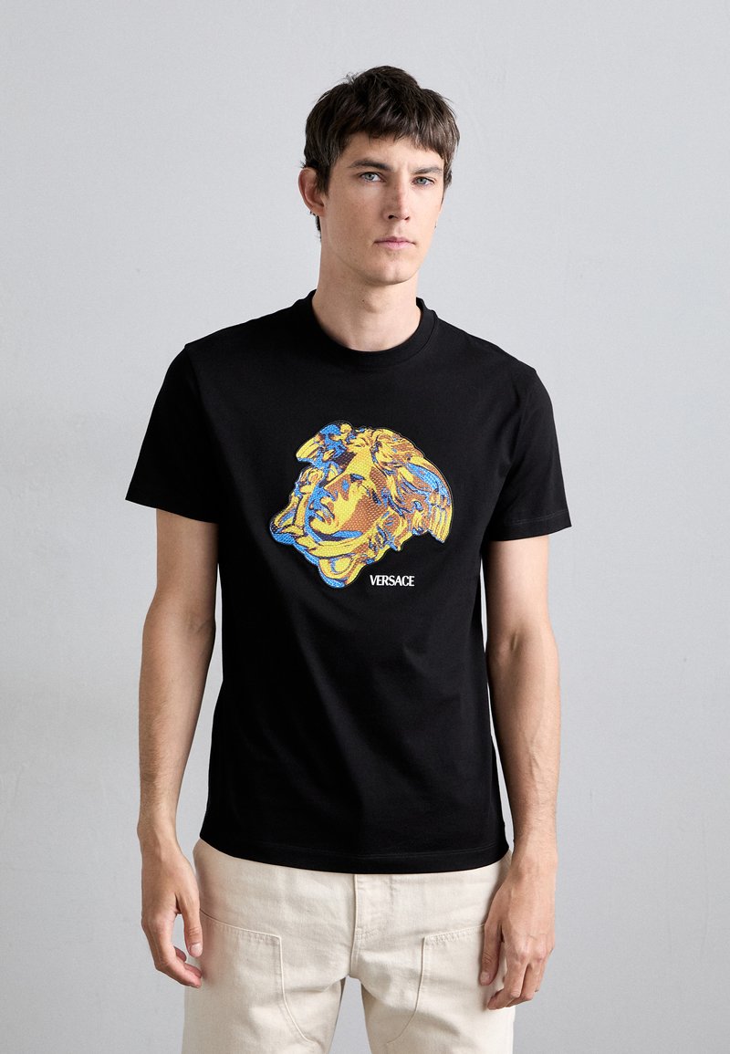 T-shirt preta de algodão com uma estampa gráfica multicolorida de uma cabeça de Medusa e o logo "VERSACE" na frente. Mangas curtas, gola redonda.