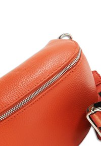 Sac en cuir avec une surface texturée orange, doté d'une fermeture éclair argentée et d'une sangle colorée à motifs, conçu en forme incurvée.