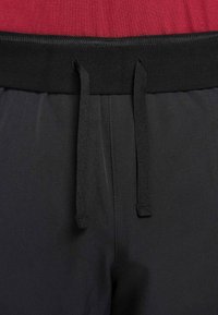 Gros plan sur une ceinture noire à cordon sur un pantalon gris foncé avec des coutures cousues et une partie d'un haut rouge au-dessus de la taille.