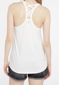 Top senza maniche bianco con design a incrocio sulla schiena, realizzato in tessuto morbido, abbinato a pantaloni shorts in denim scuri arrotolati.