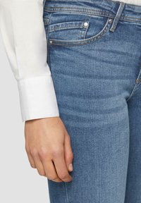 Lichtblauwe denim jeans met een slim fit, met voorzakken, subtiele stiksels en een wit overhemd met lange mouwen zichtbaar bij de pols.