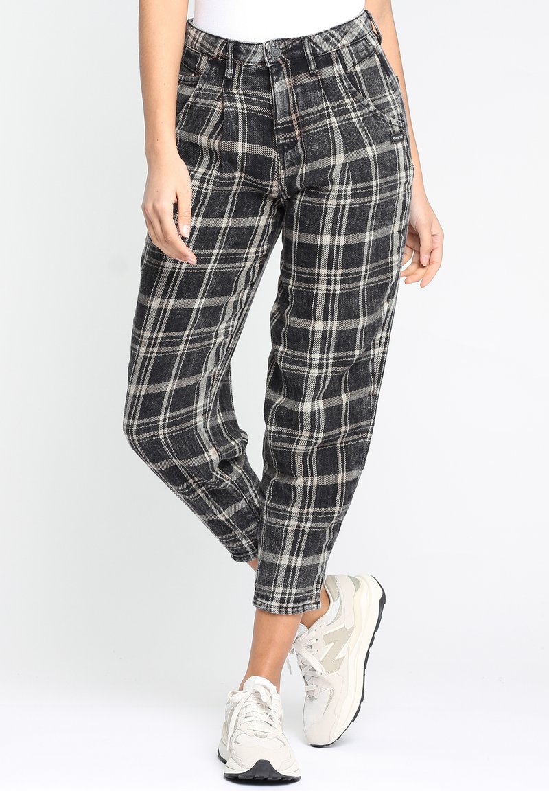 Schwarz-weiße karierte Hose mit lockerer Passform, hoher Taille, Seitentaschen und gekrempelten Säumen. Kombiniert mit hellen Sneakern.