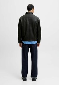 Black leather jacket with a high collar, featuring long sleeves and side zip details, worn over a light blue denim shirt and dark wide-leg jeans.
